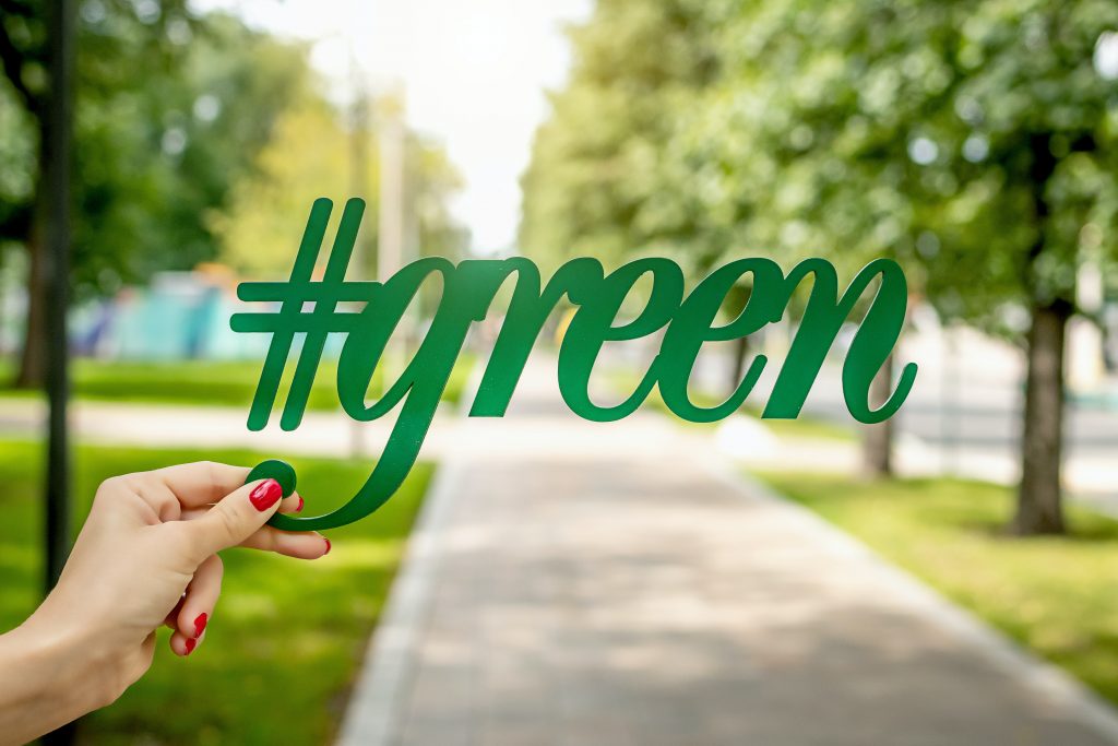 Schriftzug #green wird von einer Hand vor einer Allee gehalten